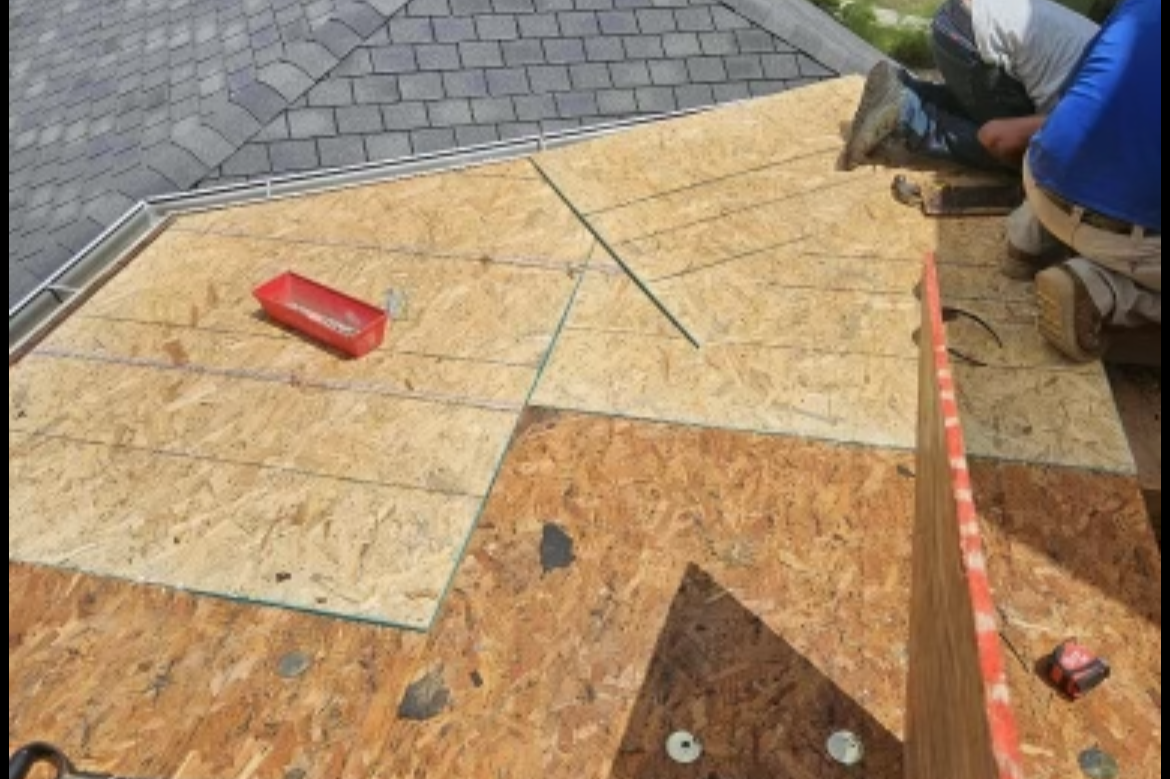 Construction workers installing plywood sheets on a roof, with tools and measuring tape visible.