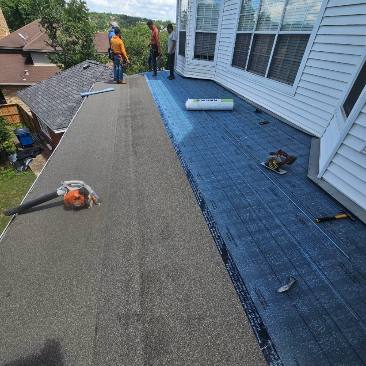 Roof repair workers installing new roofing on a house, with roofing materials and tools visible.