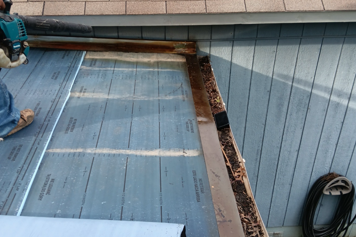 Partial view of a roof construction site showing underlayment and metal flashing along the edge of the roof.