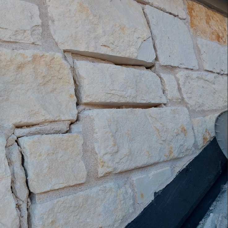 Close-up of a beige and white stone brick wall with noticeable cracks.