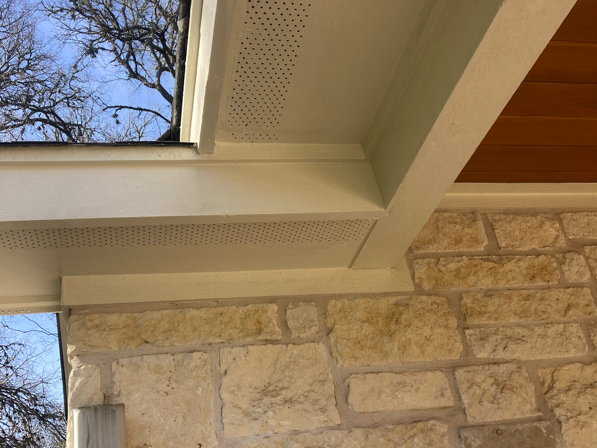 Close-up photo of a house window ledge showing wood trim, beige brick wall, and stone wall with a tree and sky visible outside.