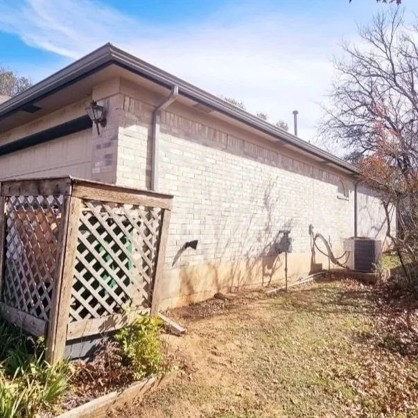 Backyard side view of a single-story brick house with a lattice privacy fence, an air conditioning unit, and clear sky.