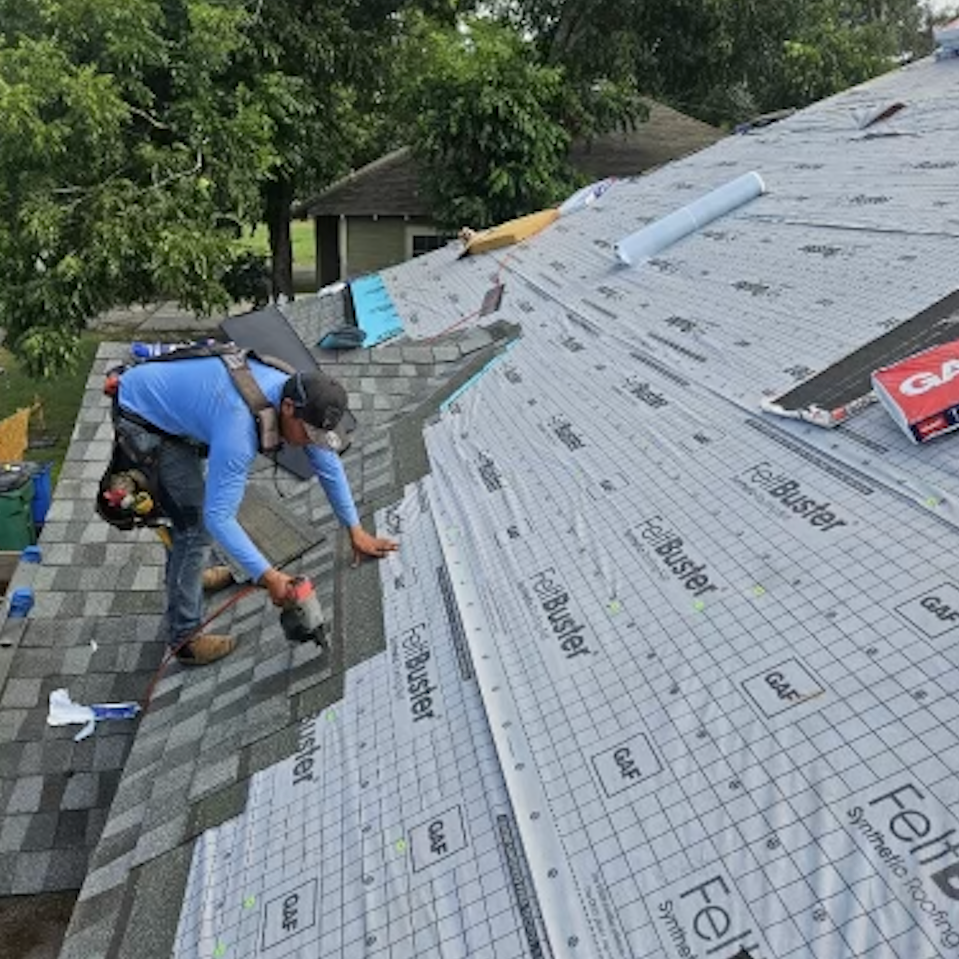 A worker installing shingles on a roof, partially covered with FelBuster roofing underlayment.