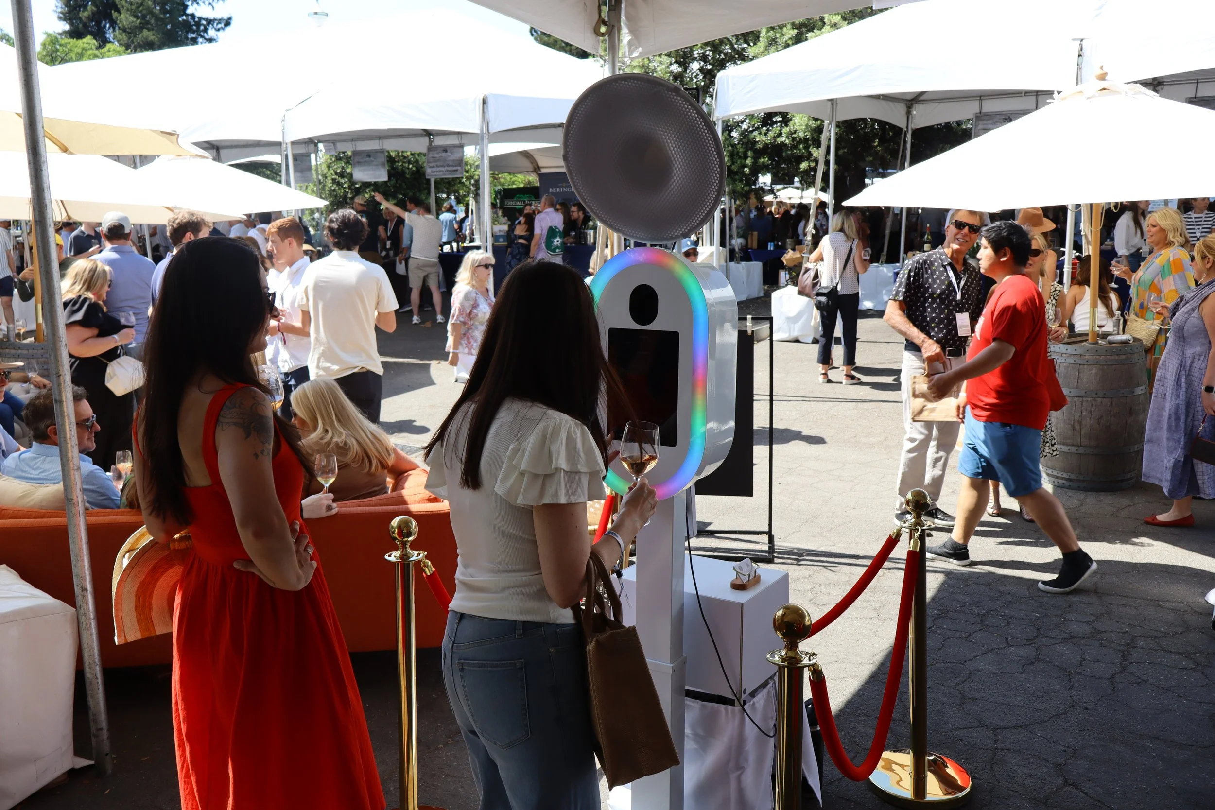 People at an outdoor event taking photos with a photo booth and socializing under tents.