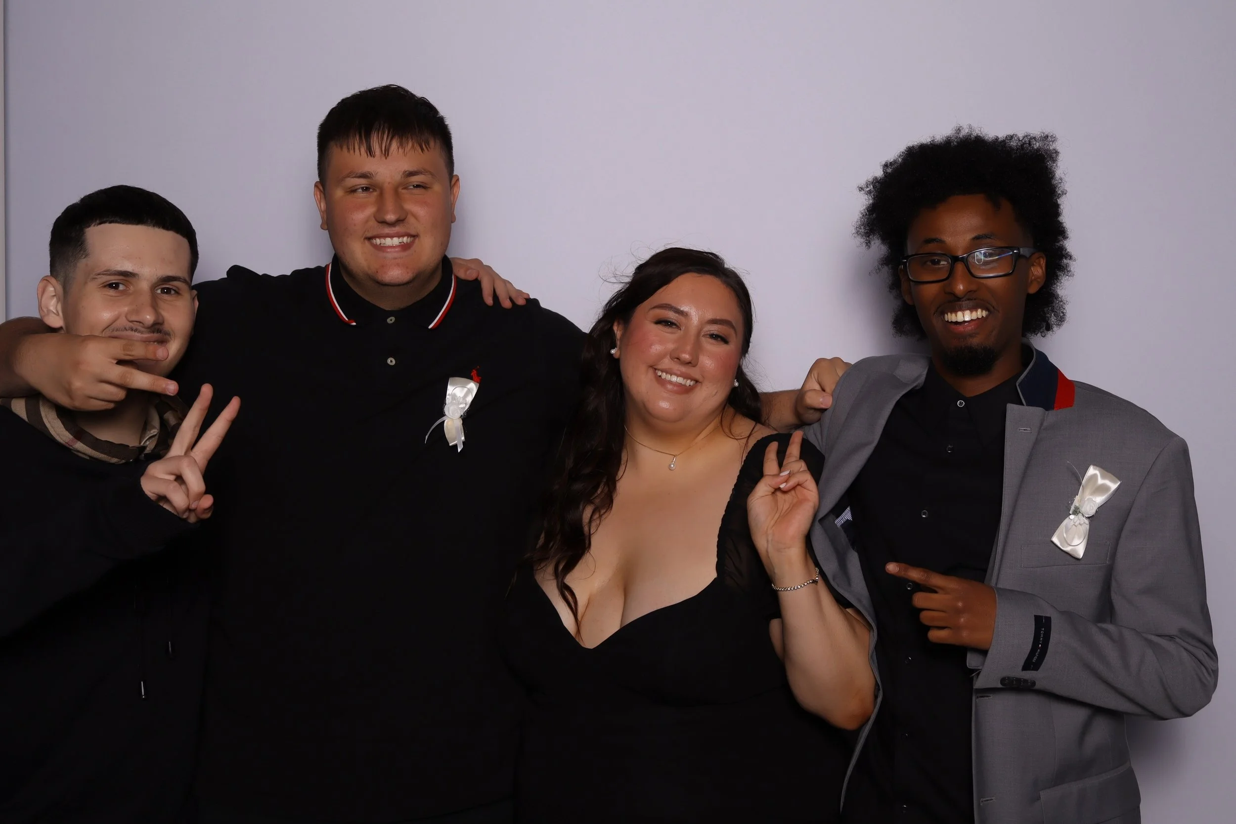 Four people smiling and posing for a photo against a plain white background, with some making peace signs and pointing.