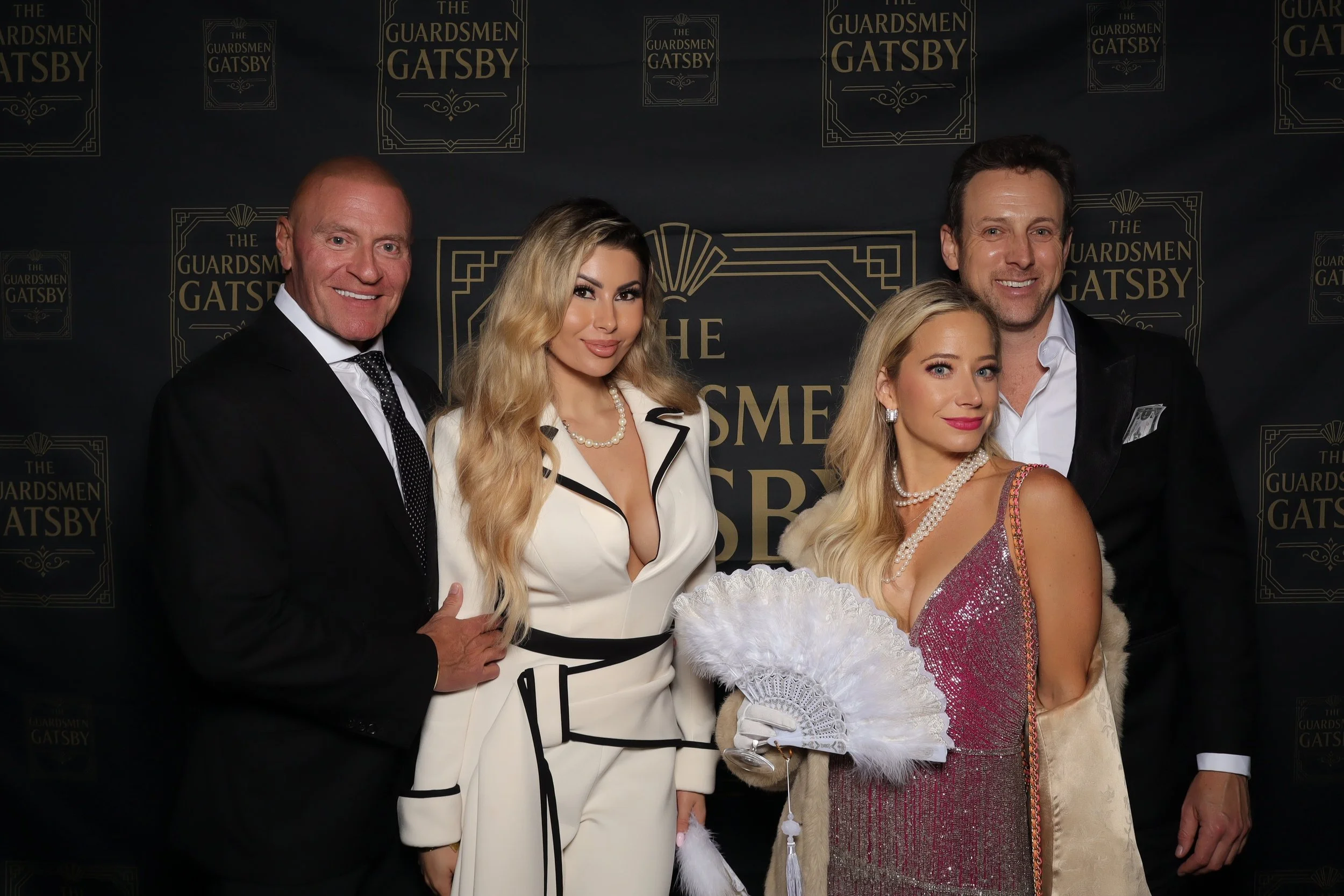 Four people posing for a photo at a Gatsby-themed event, with a backdrop reading 'The Guardsmen Gatsby'.