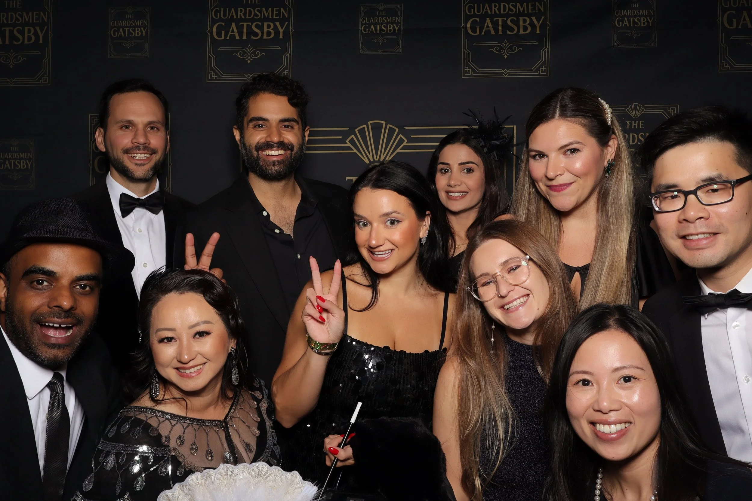 Group of people dressed in formal attire at a Gatsby-themed event, with a backdrop featuring the words 'The Guardsmen Gatsby'.