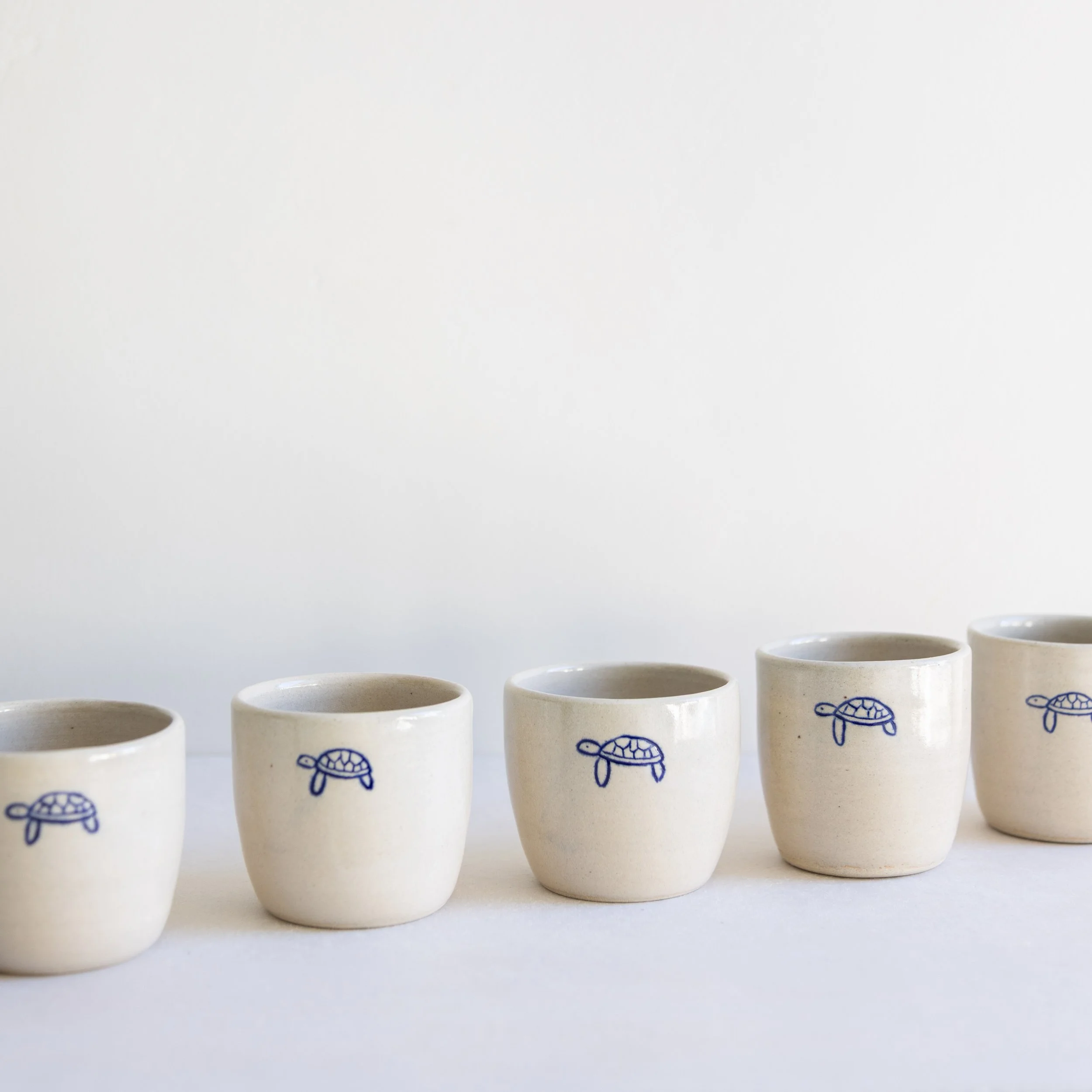 Handmade sandy-coloured espresso cups with a hand-drawn turtle design.