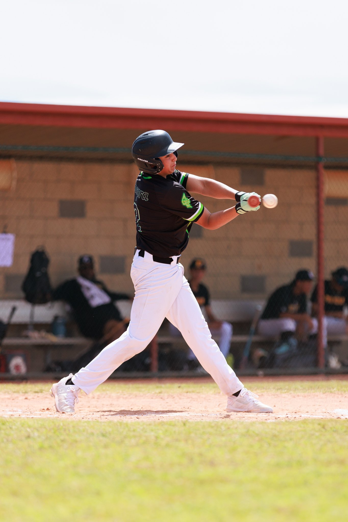 A baseball player swinging a bat during a game, wearing a black helmet and uniform, on a sunny day at a baseball field.