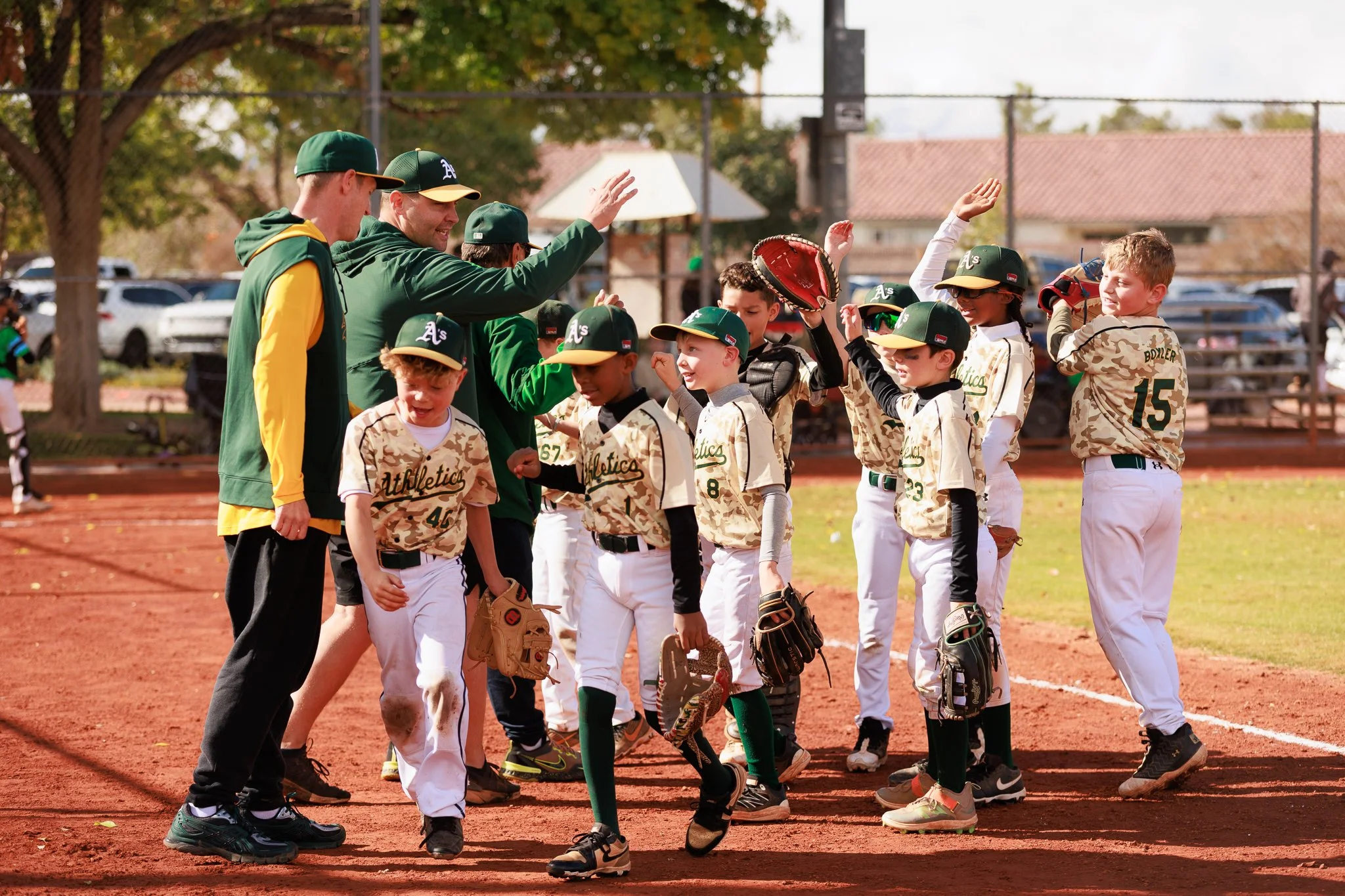 Youth baseball players and coaches on the field, some with their hands raised for a high five after a game.