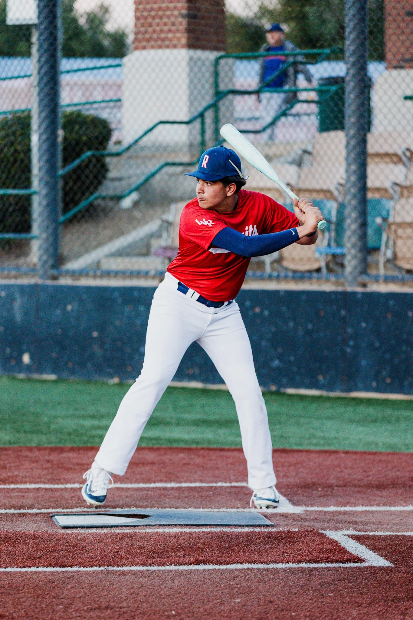Baseball player in red jersey and white pants batting at a tee on a baseball field.