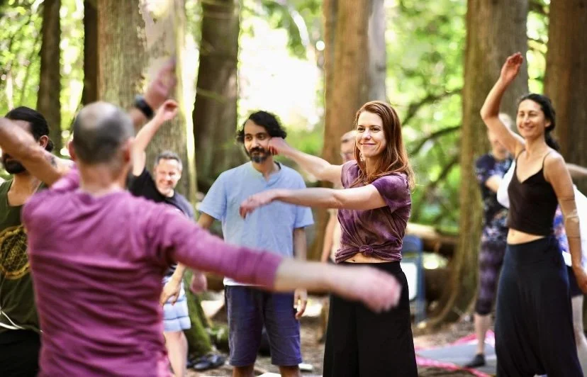 People dancing together in a forest with tall trees and green foliage, enjoying an outdoor gathering or dance event.