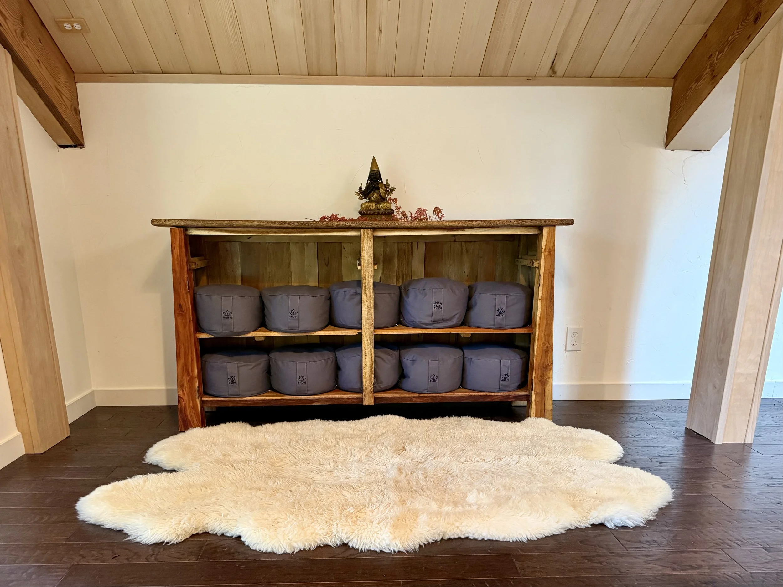 Wooden shelf with six gray water bottles on a shelf, placed on a fluffy beige rug in a room with wooden ceiling and floors.