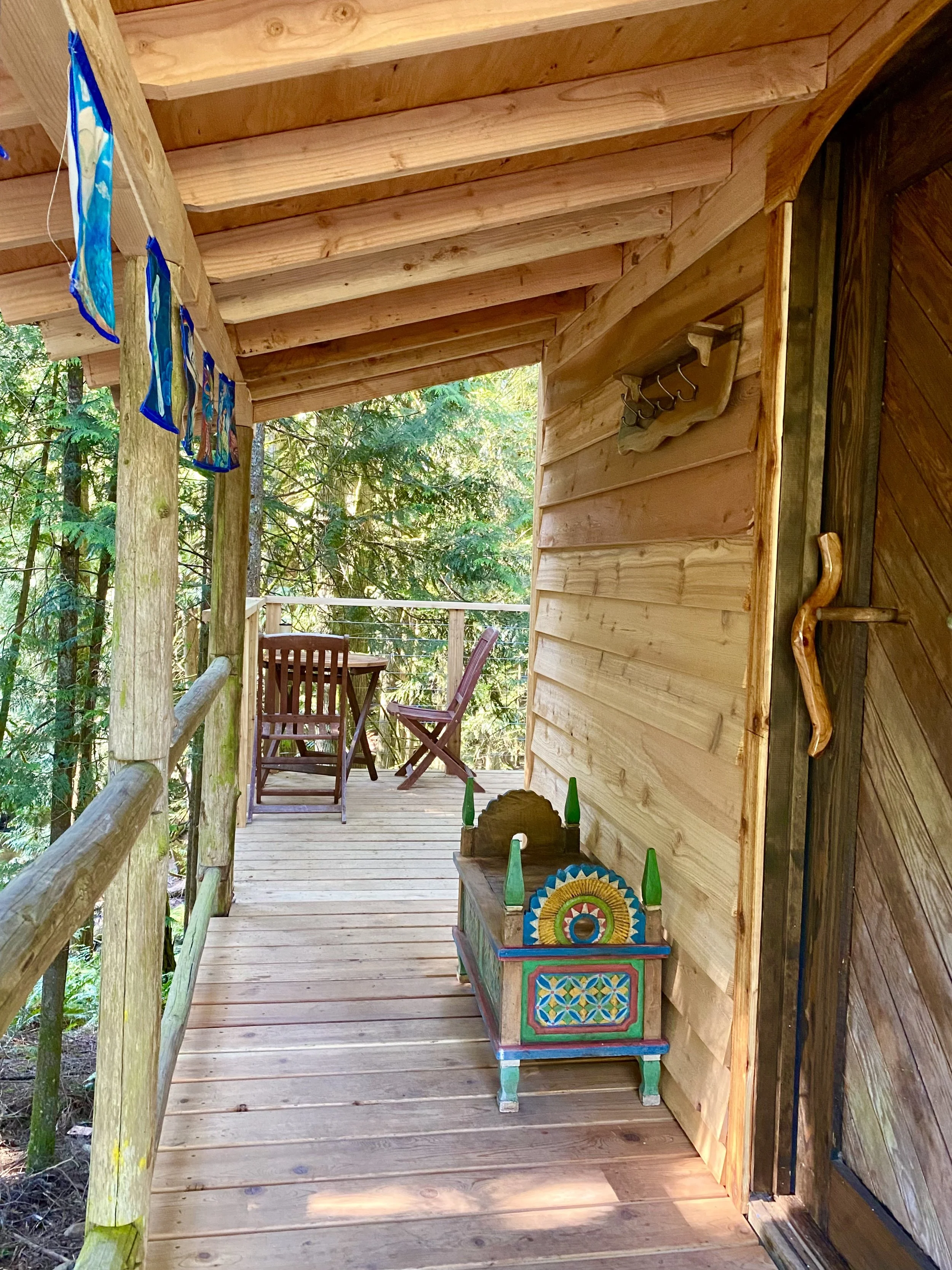 Wooden porch with outdoor furniture and colorful decorative chest, overlooking a forested area.