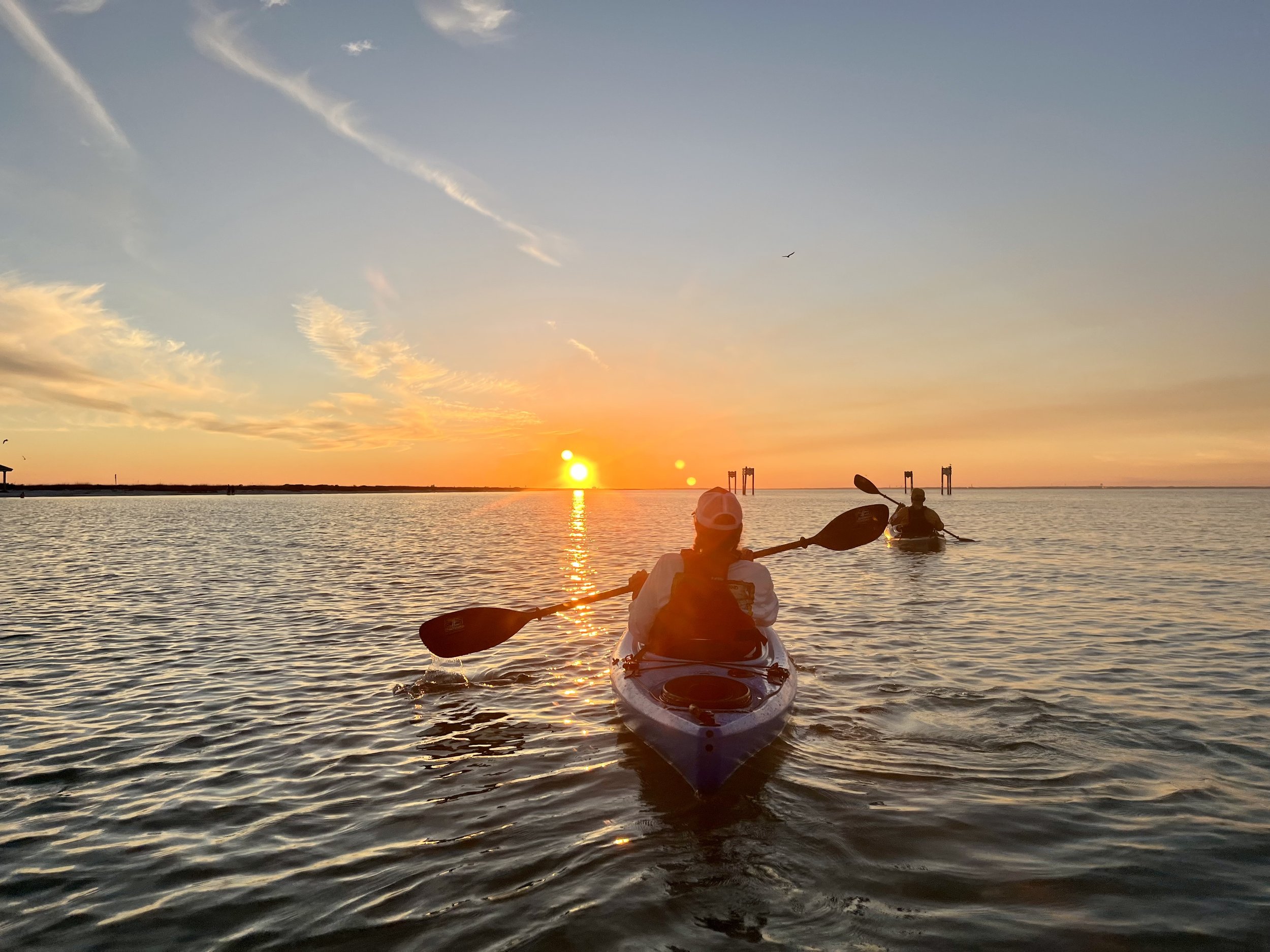Two kayaks on a sandy beach during sunset, with waves in the ocean and a glowing orange sky.