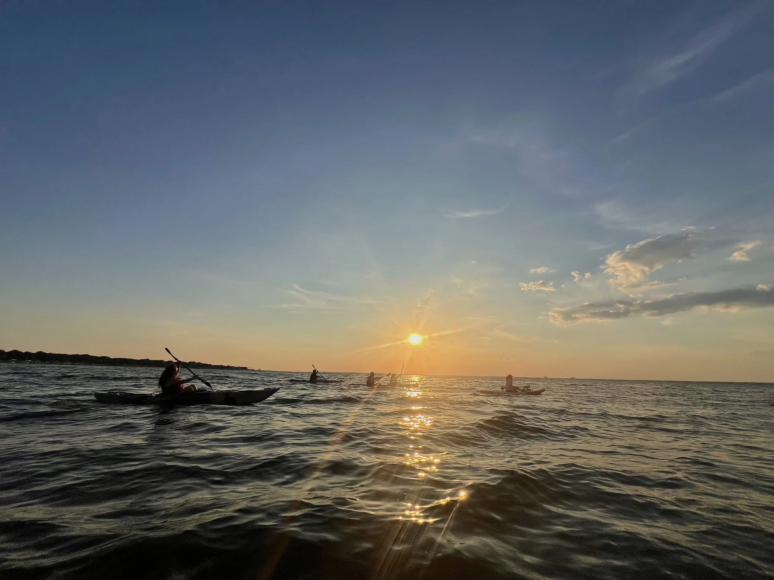 People kayaking on a body of water during sunset with a clear sky and some clouds