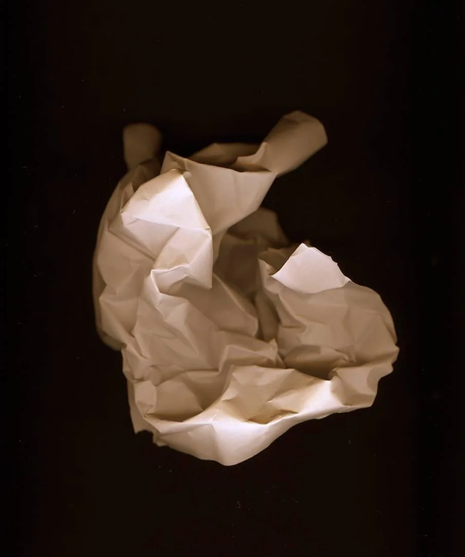 Crumpled white paper resting on a surface, evoking the creative process and discarded drafts.