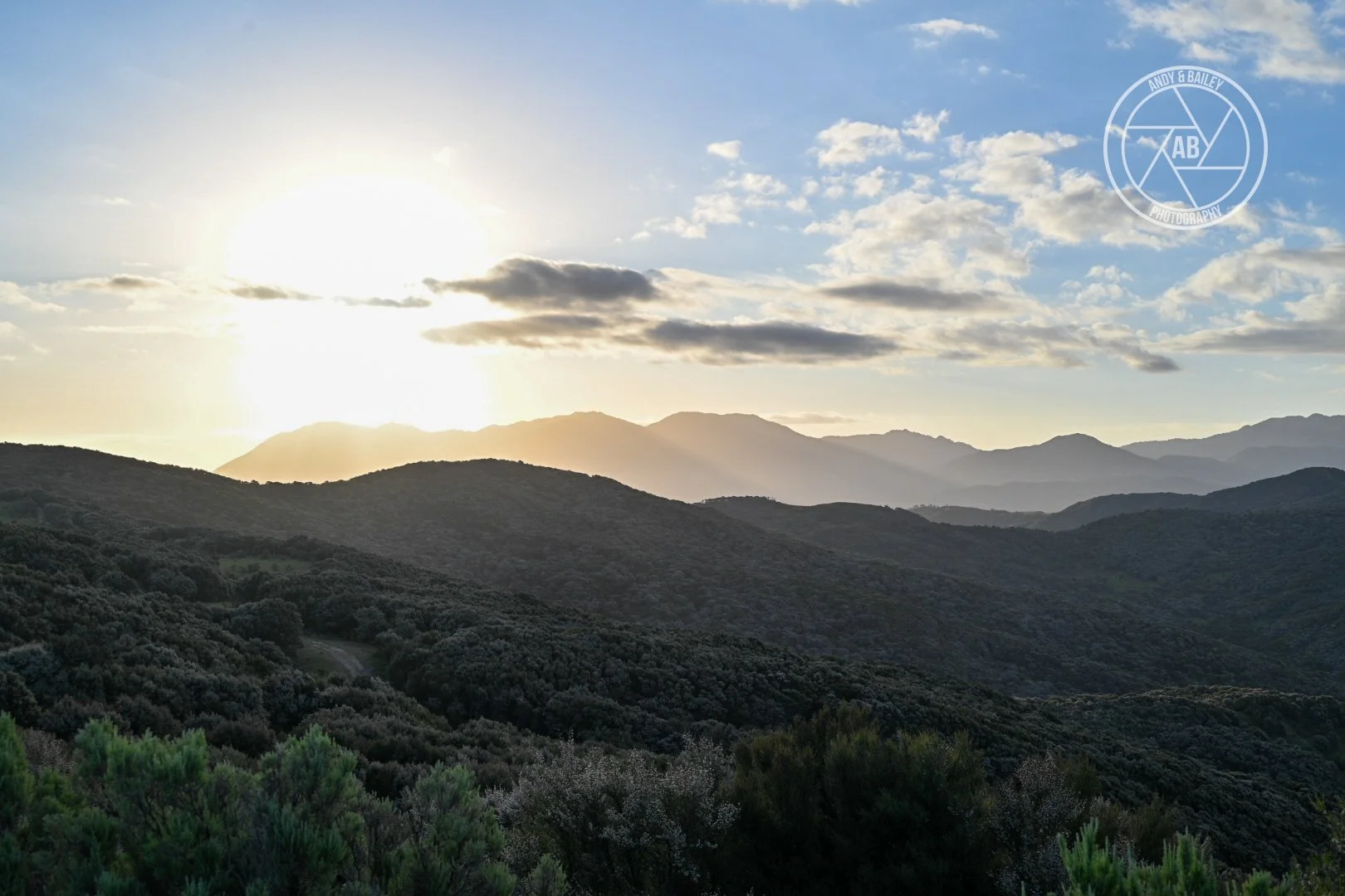 Sunset over rolling green mountains with a partly cloudy sky, The Last Resort, Wairarapa.