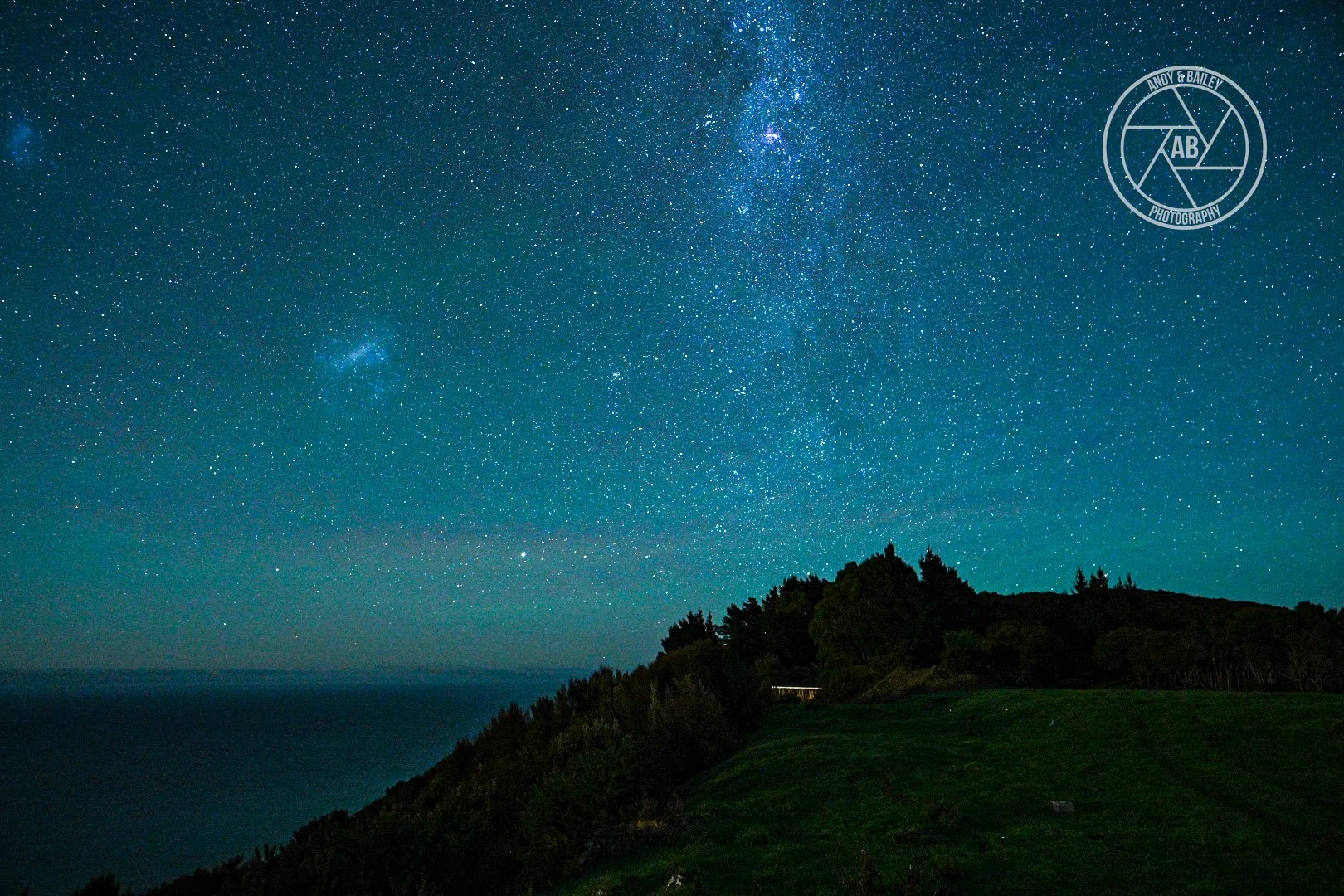 Nighttime sky filled with stars above a dark green hillside and ocean.