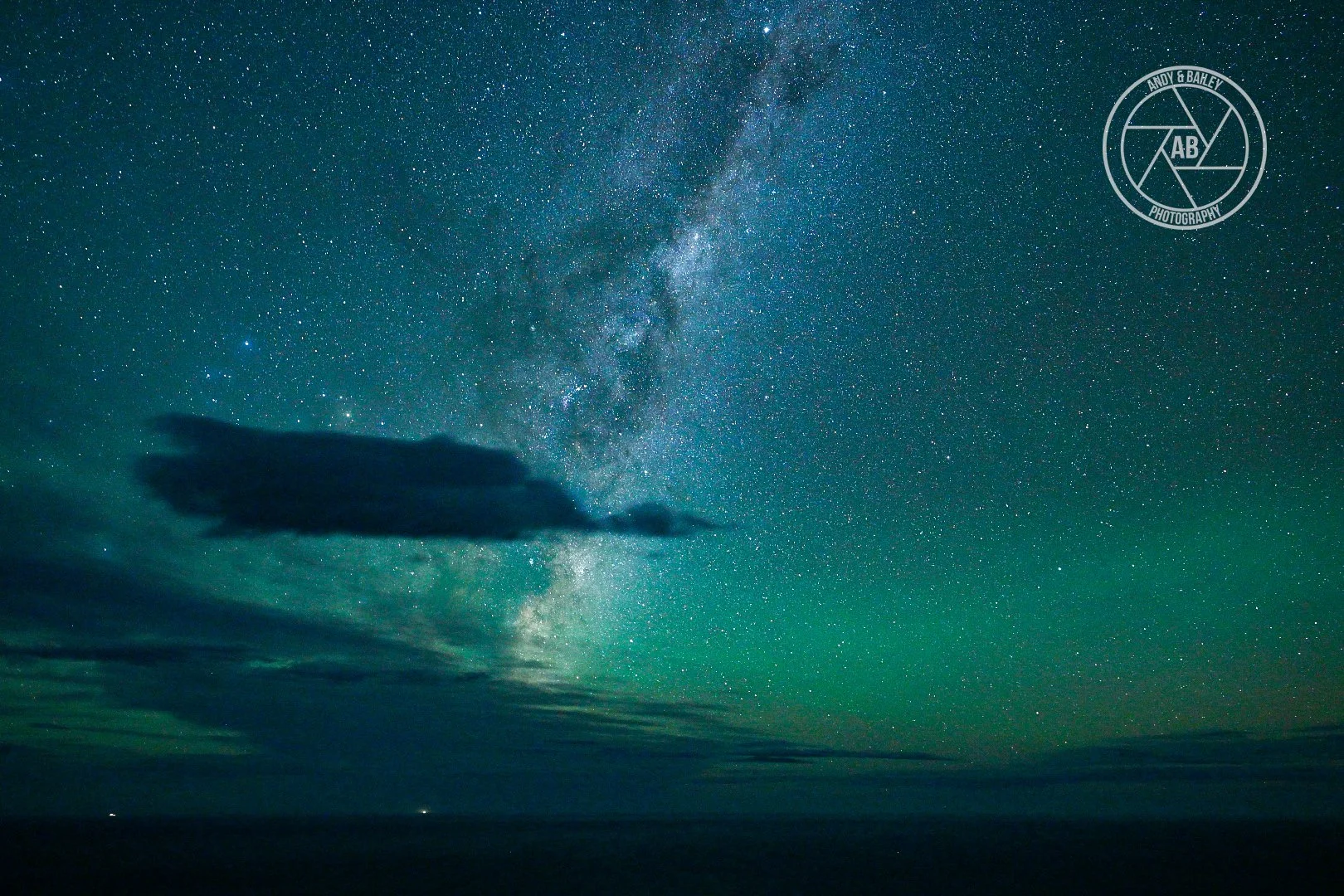 Night sky filled with stars and the Milky Way galaxy, with some clouds and a calm horizon.