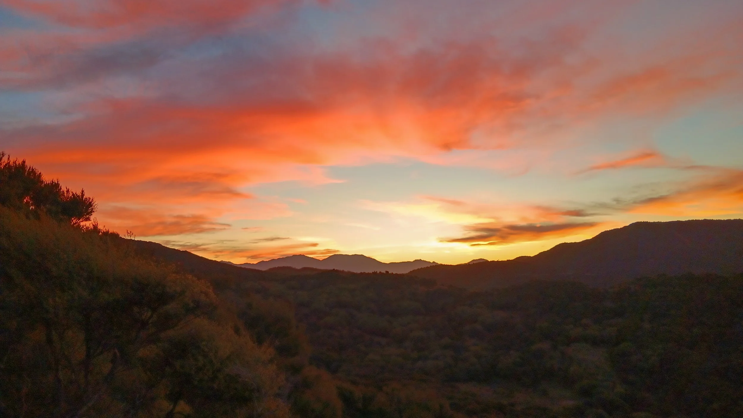 Sunset over a mountainous landscape with colorful pink, orange, and blue clouds in the sky.