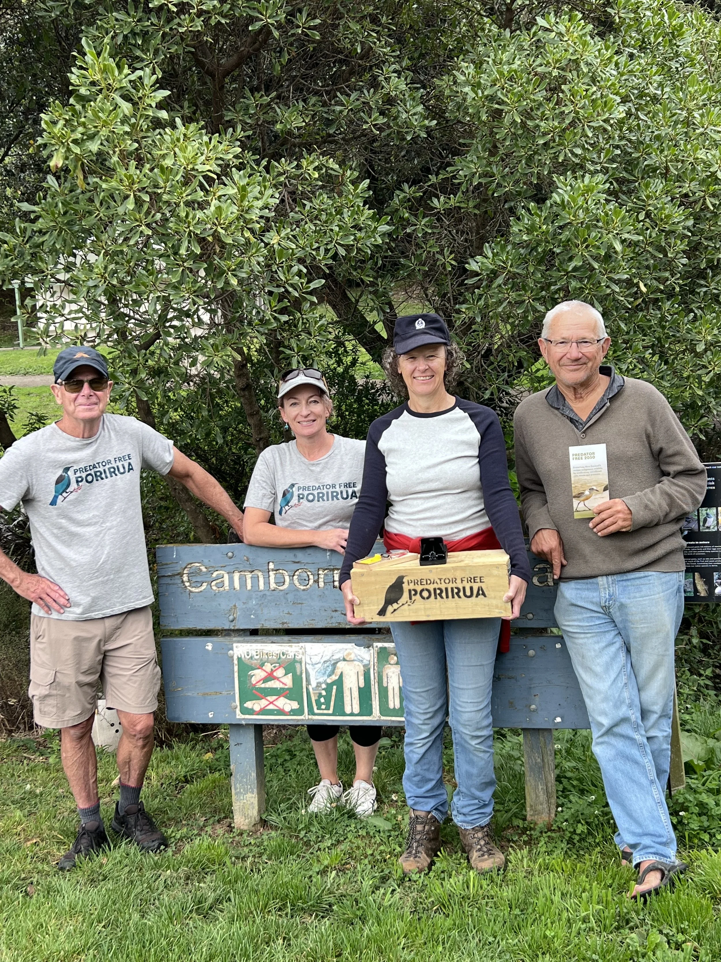 Group of people in bright vests posing by Camborne Walkway sign, with trees and shrubbery in the background.