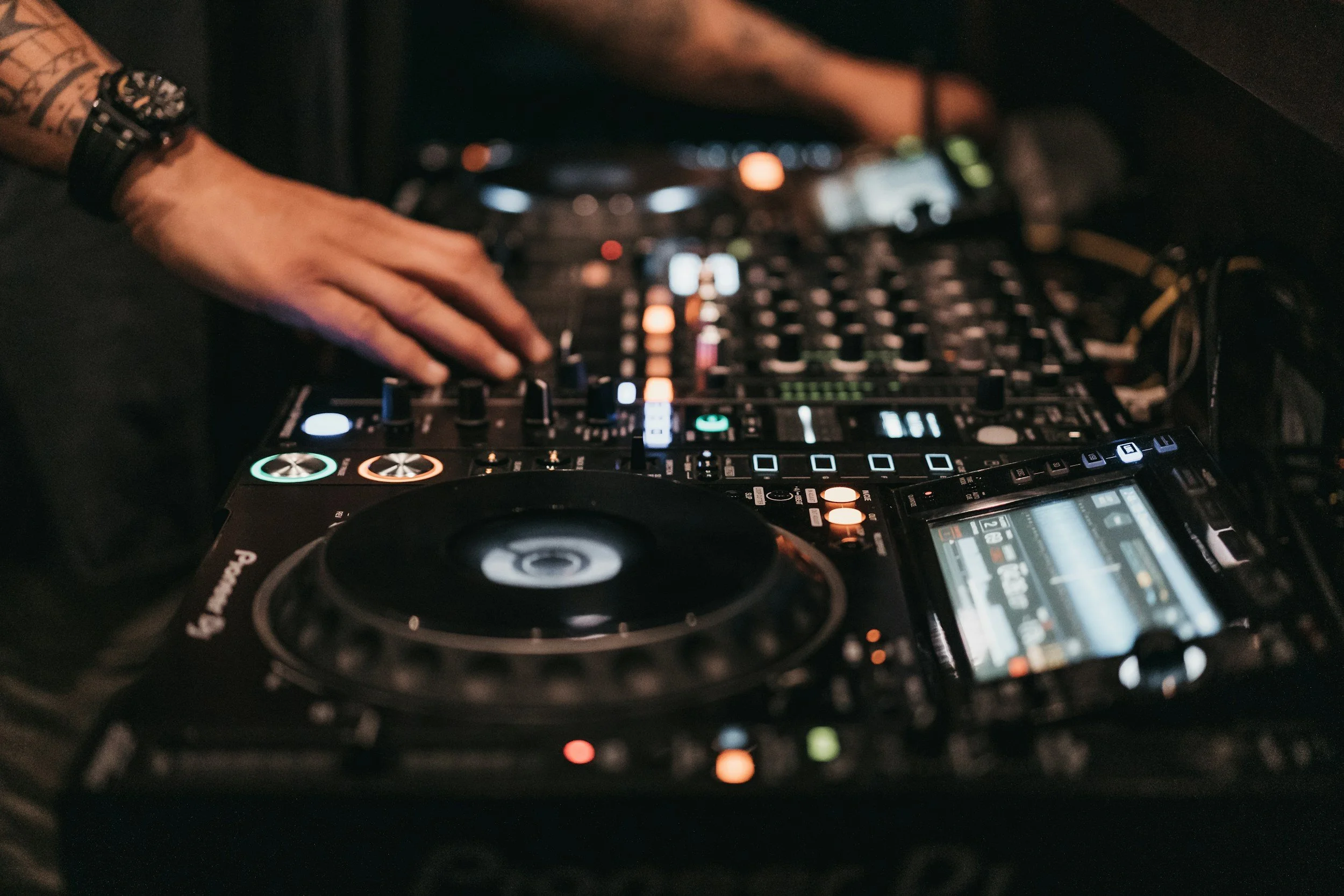 Manos de DJ manipulando una consola de mezcla con botones iluminados y pantallas LED.