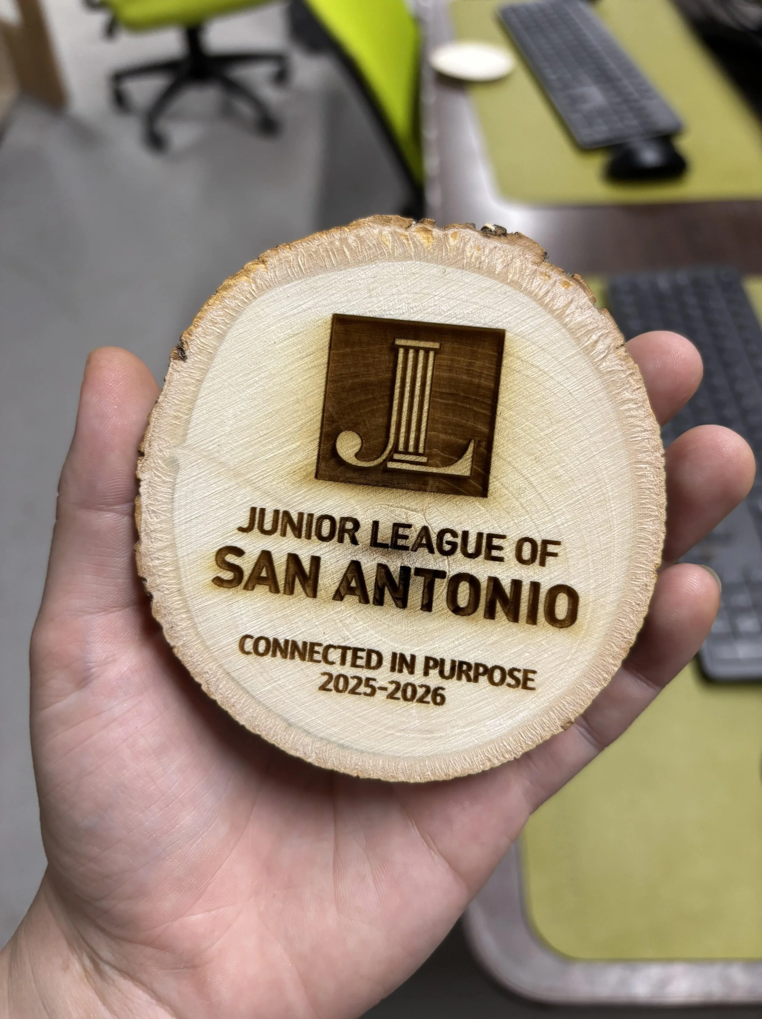 A wooden plaque with engraved text that reads 'Junior League of San Antonio, Connected in Purpose, 2025-2026' and a logo with a stylized letter J.