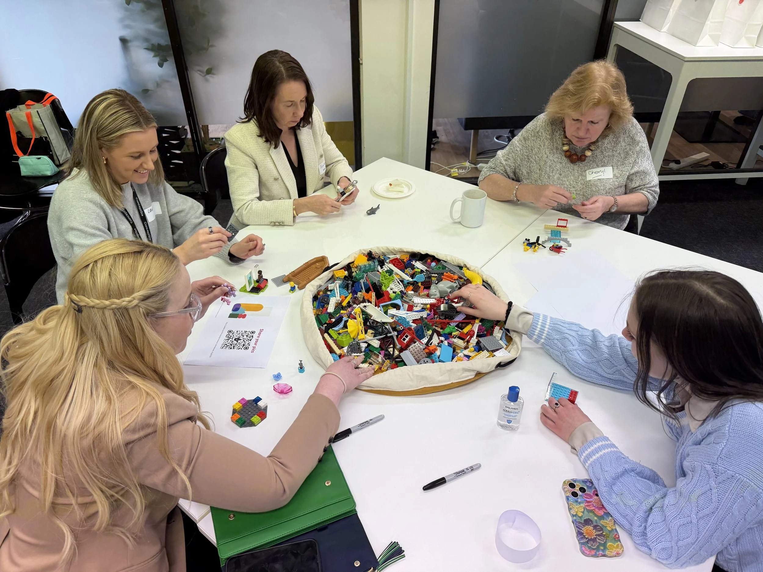 Five people sitting around LEGO bricks at a table building models