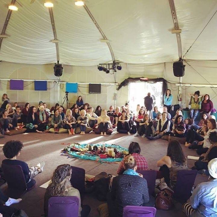 People sitting in a large circle inside a tent at WisdomWomen Visionary Gathering at Esalen Institute. They are participating in a group activity and discussion.