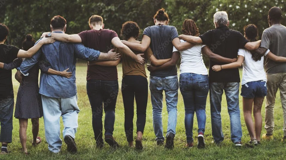 A diverse group of people standing together outdoors, embracing and walking away from the camera.