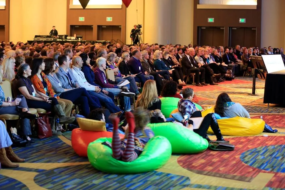 Large conference room filled with seated audience and some children sitting and lying on colorful bean bags near the front. Taken at a Wisdom 2.0 Conference in San Francisco, CA.