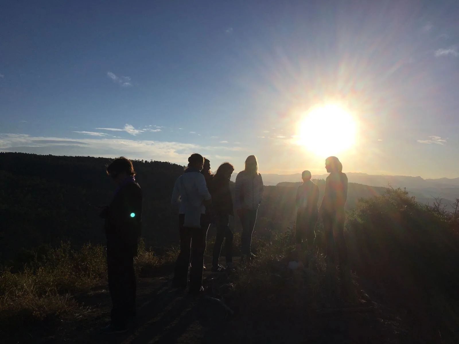Group of people standing outdoors during a Colorado sunset or sunrise on a mountain near Tara Mandala Retreat Center, with a scenic view of the landscape in the background.
