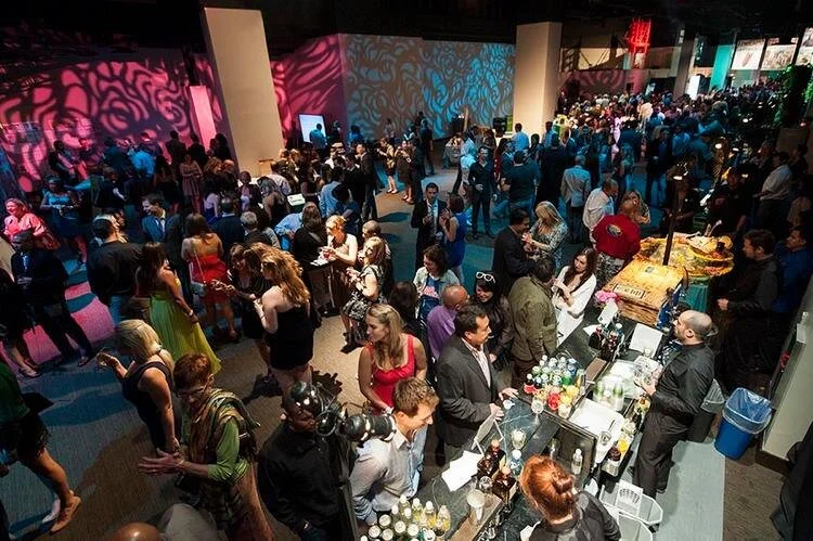 Crowd of people at a crowded event or party with colorful lighting and a bar area.