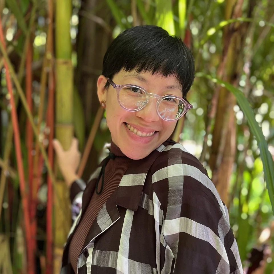 LiZhen Wang headshot with short black hair, glasses, and a striped jacket smiling outdoors in a lush green bamboo forest.