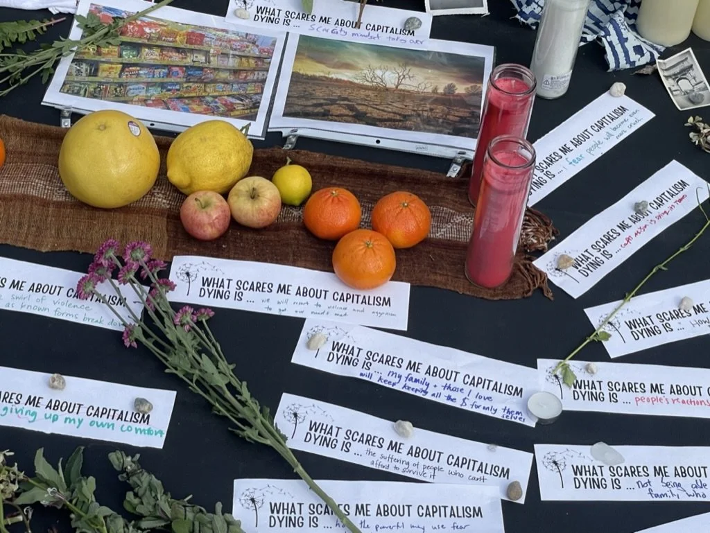 A display table with fruit, flowers, posters, and papers discussing concerns about capitalism and climate change.