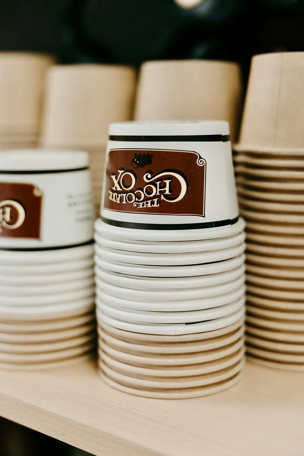 Stacks of disposable coffee cups with a brown and white design on a shelf.