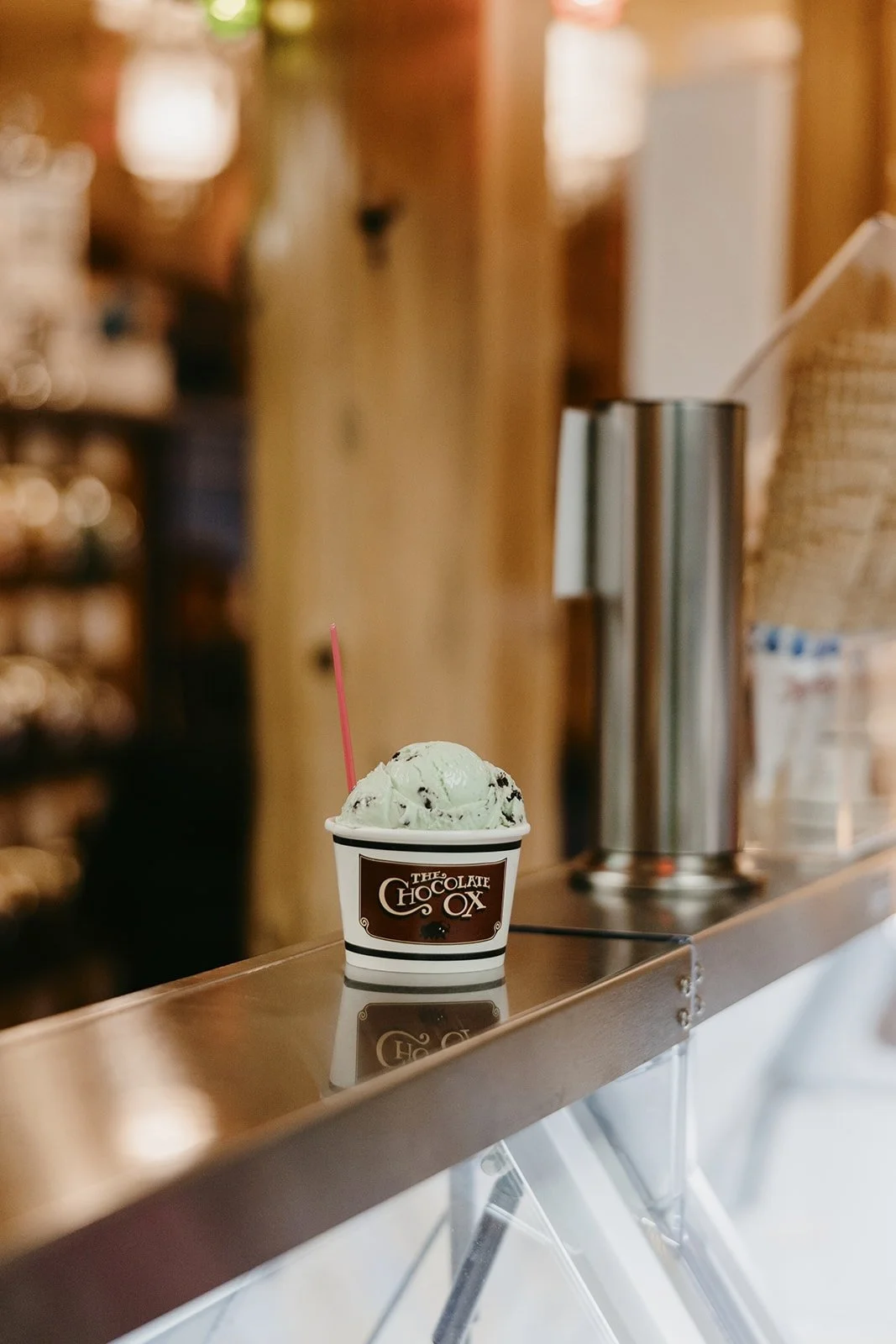 Mint chocolate chip ice cream in a cup with a spoon, on a counter at a dessert shop.