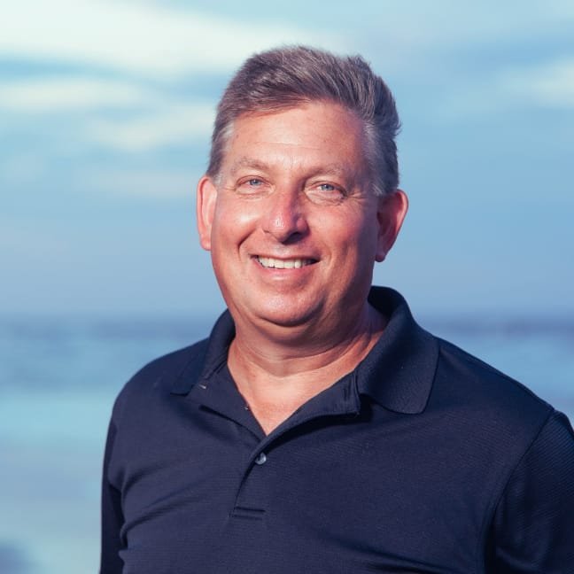 Dave Morris College Athletic Advisor smiling outdoors with a cloudy sky and ocean in the background.