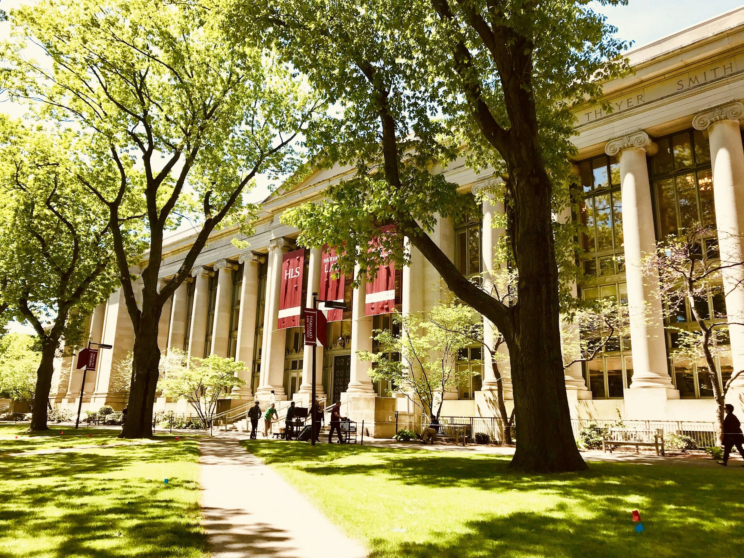 Harvard Law School building with classical columns, red banners, and surrounded by green trees and grass.