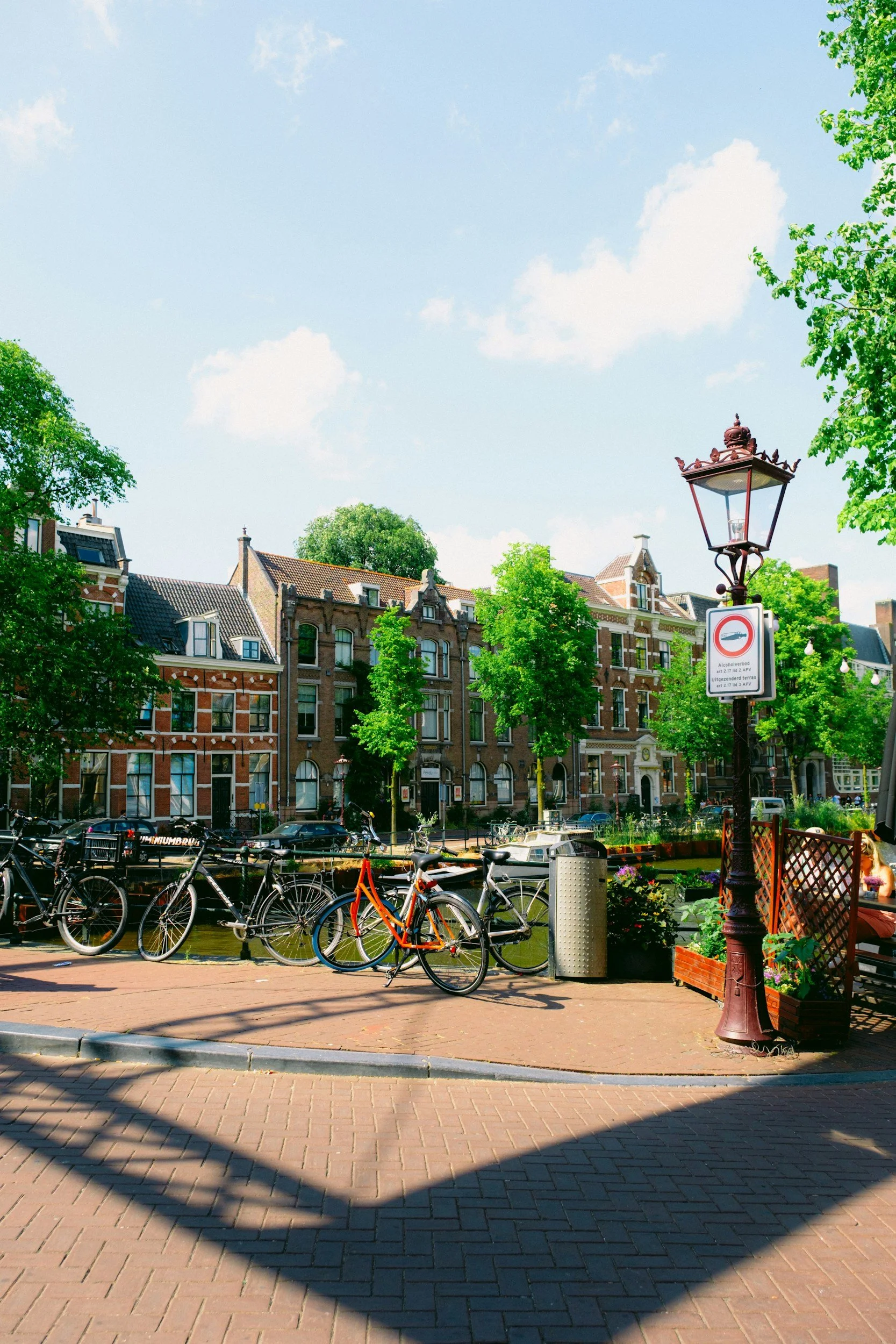 Student bicycles parked along a canal in Leiden with historic brick buildings, trees, and a decorative streetlamp.