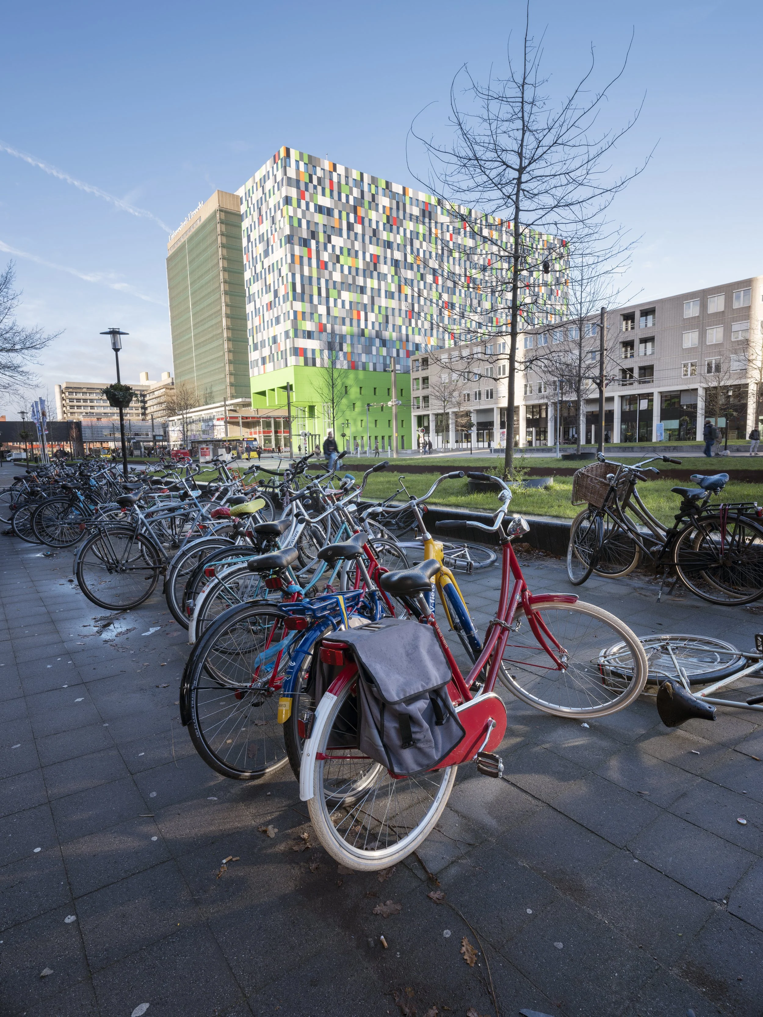 Bicycles parked on a sidewalk at Utrecht university, and a colorful modern building with a green base and a panel-faceted facade in an urban setting.