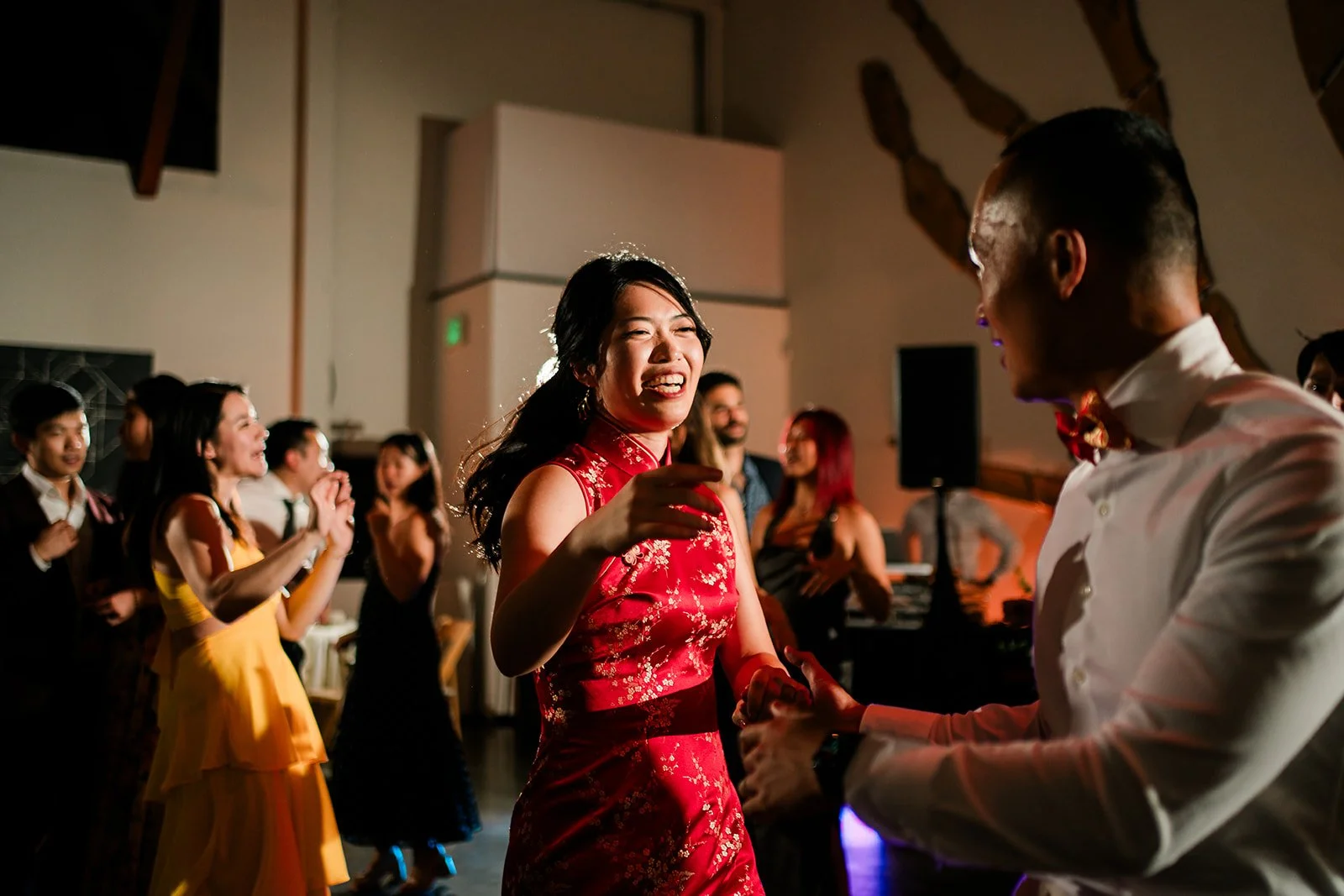 People dancing and celebrating at a wedding at The Pearl SF, with two central figures holding hands and smiling.
