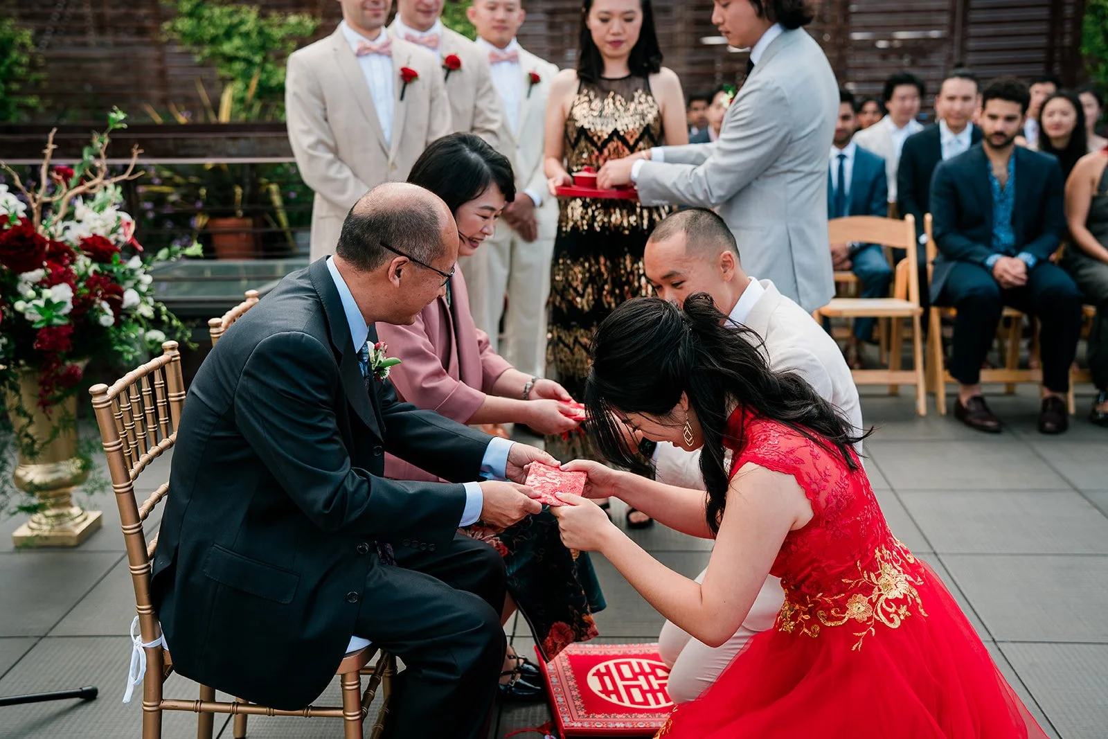 A traditional Chinese wedding ceremony with bride and groom exchanging red envelopes, surrounded by family and friends.