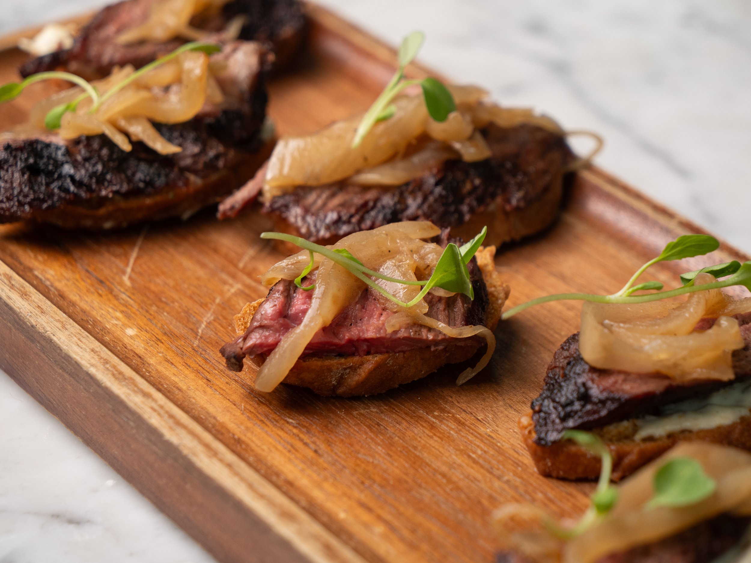 Close-up of grilled steak topped with caramelized onions and microgreens on a wooden cutting board.