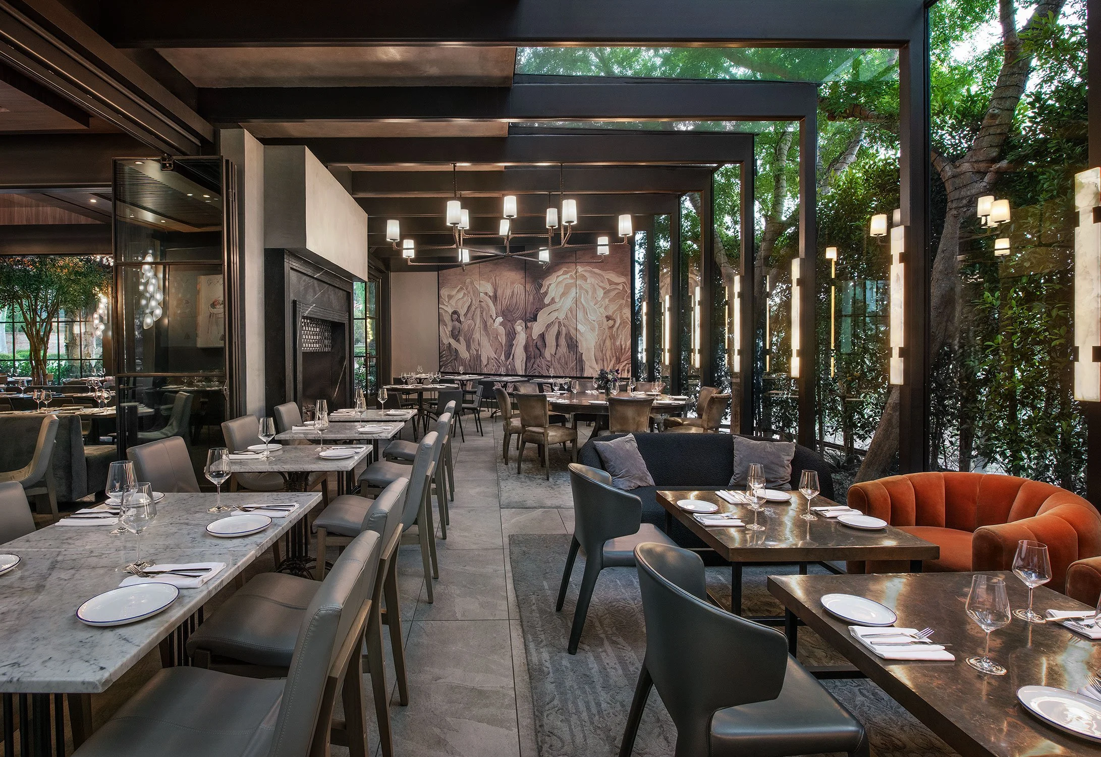 Elegant restaurant interior with large windows, modern lighting fixtures, and a mix of marble and wood surfaces, set with tables, glassware, and chairs.