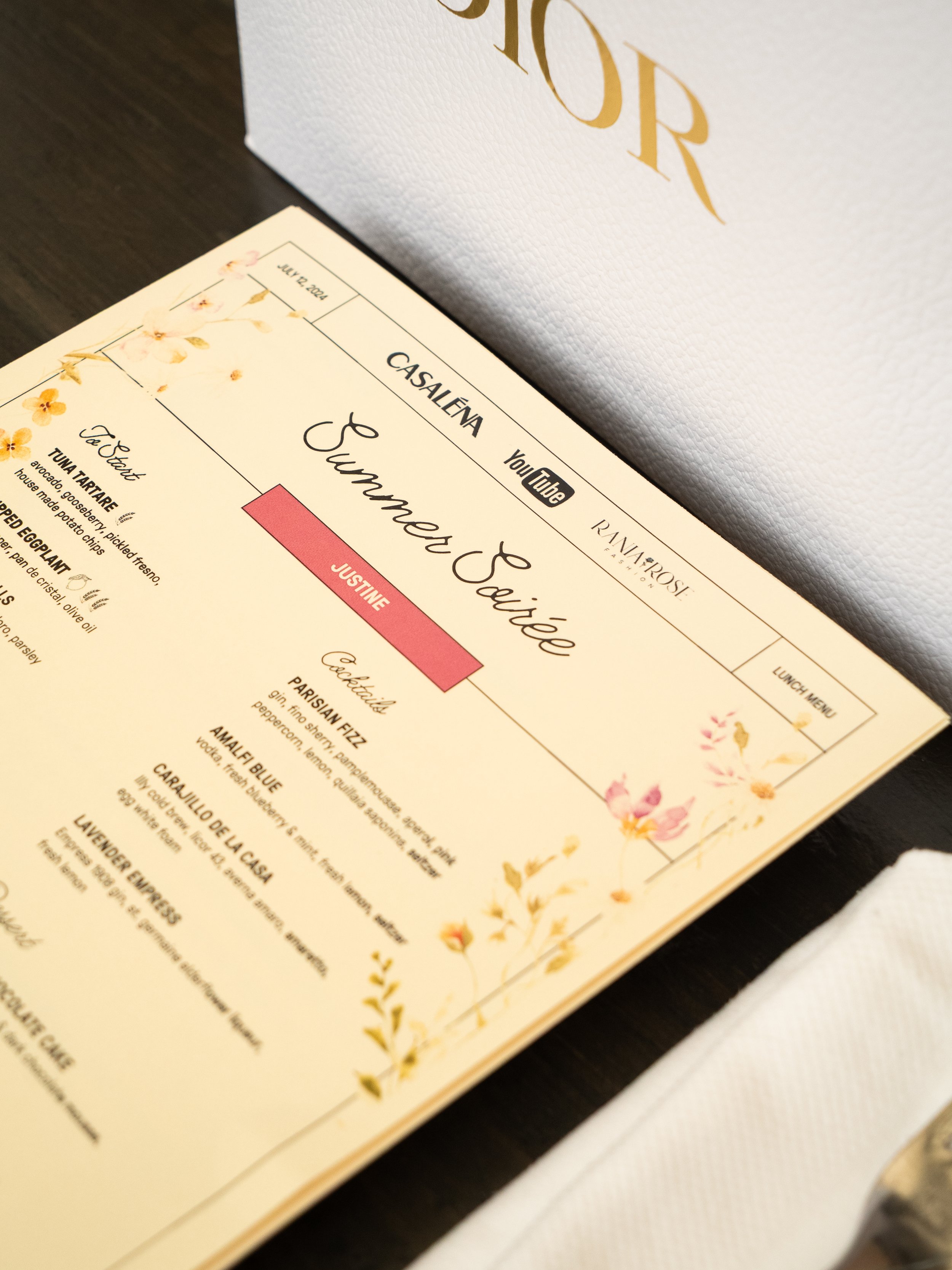 A wedding menu with floral design and the name 'Sunflower Say I Do' printed on it, resting on a dark surface with a white textured background.