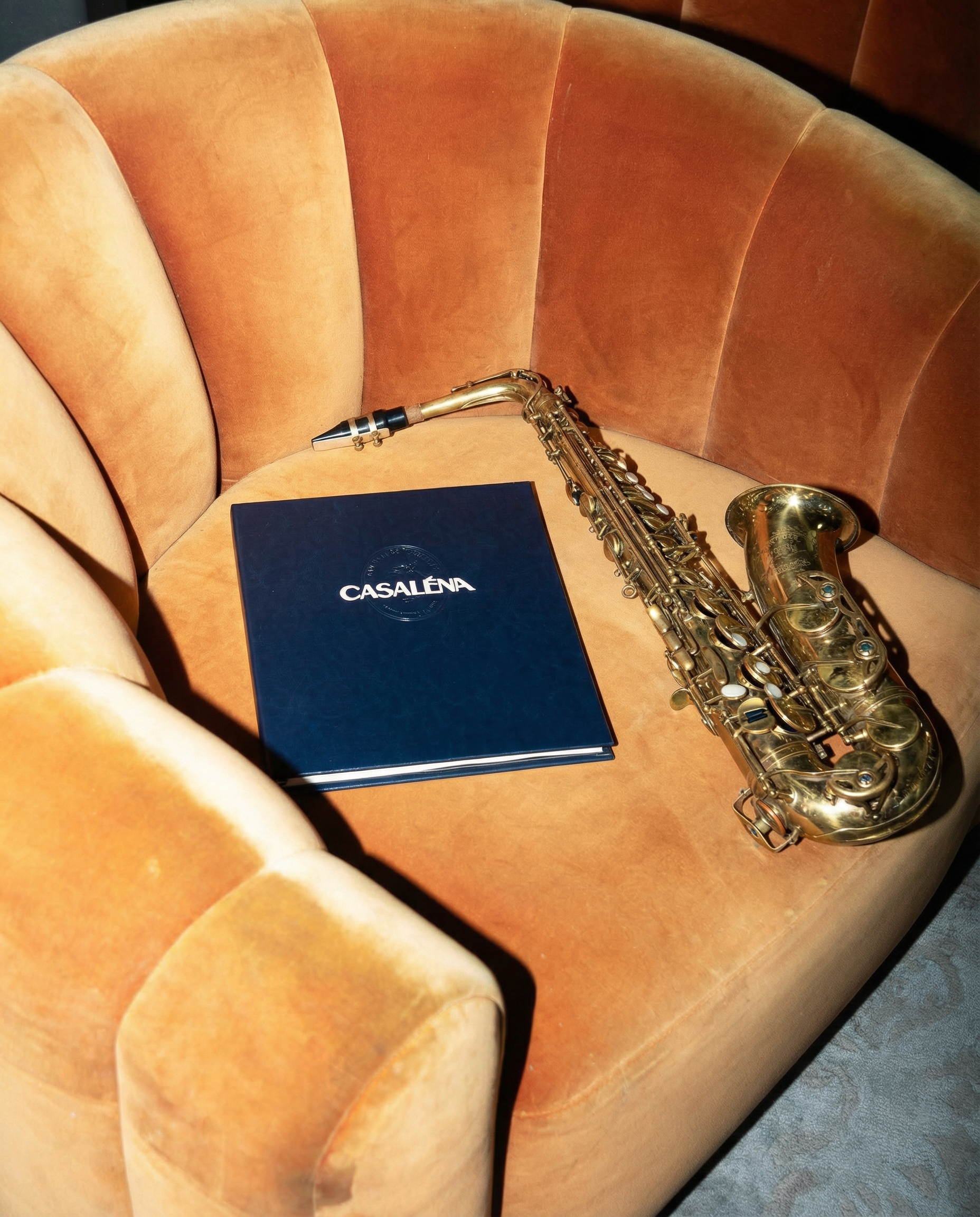 a saxophone lays on a velvet chair next to a Casaléna menu