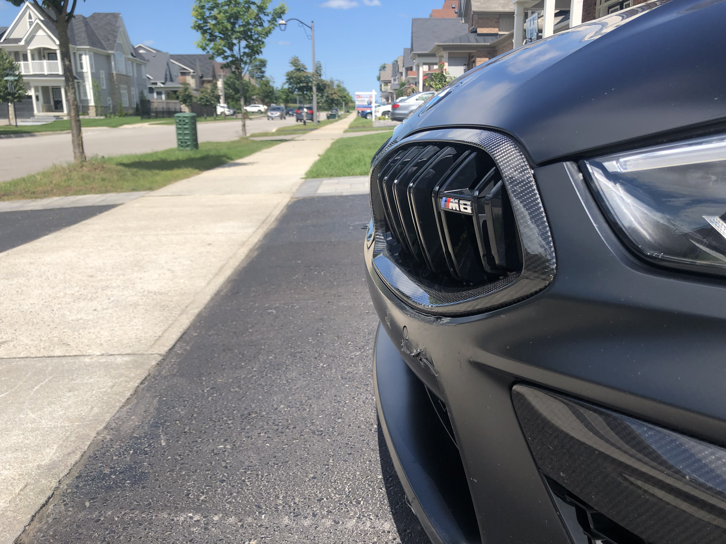 Close-up of a black BMW M6 front grille and headlight on a suburban street.