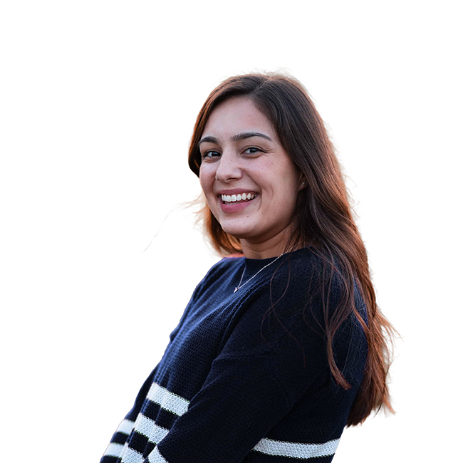 Abby Castillo with long brown hair smiling at the camera, wearing a black sweater with white and black stripes.